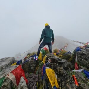 Man standing on misty Mussorie Range peak with colorful prayer flags, perfect for adventure themes.