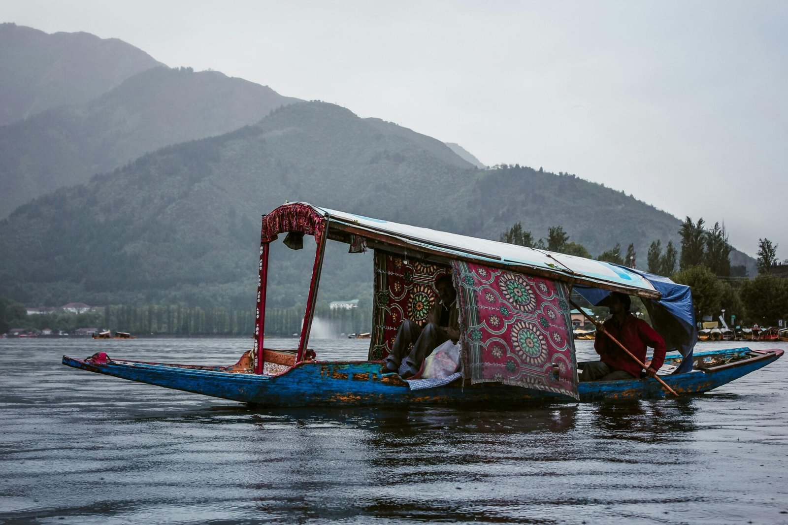 A scenic view of a shikara boat navigating Dal Lake in Srinagar, surrounded by mountains.